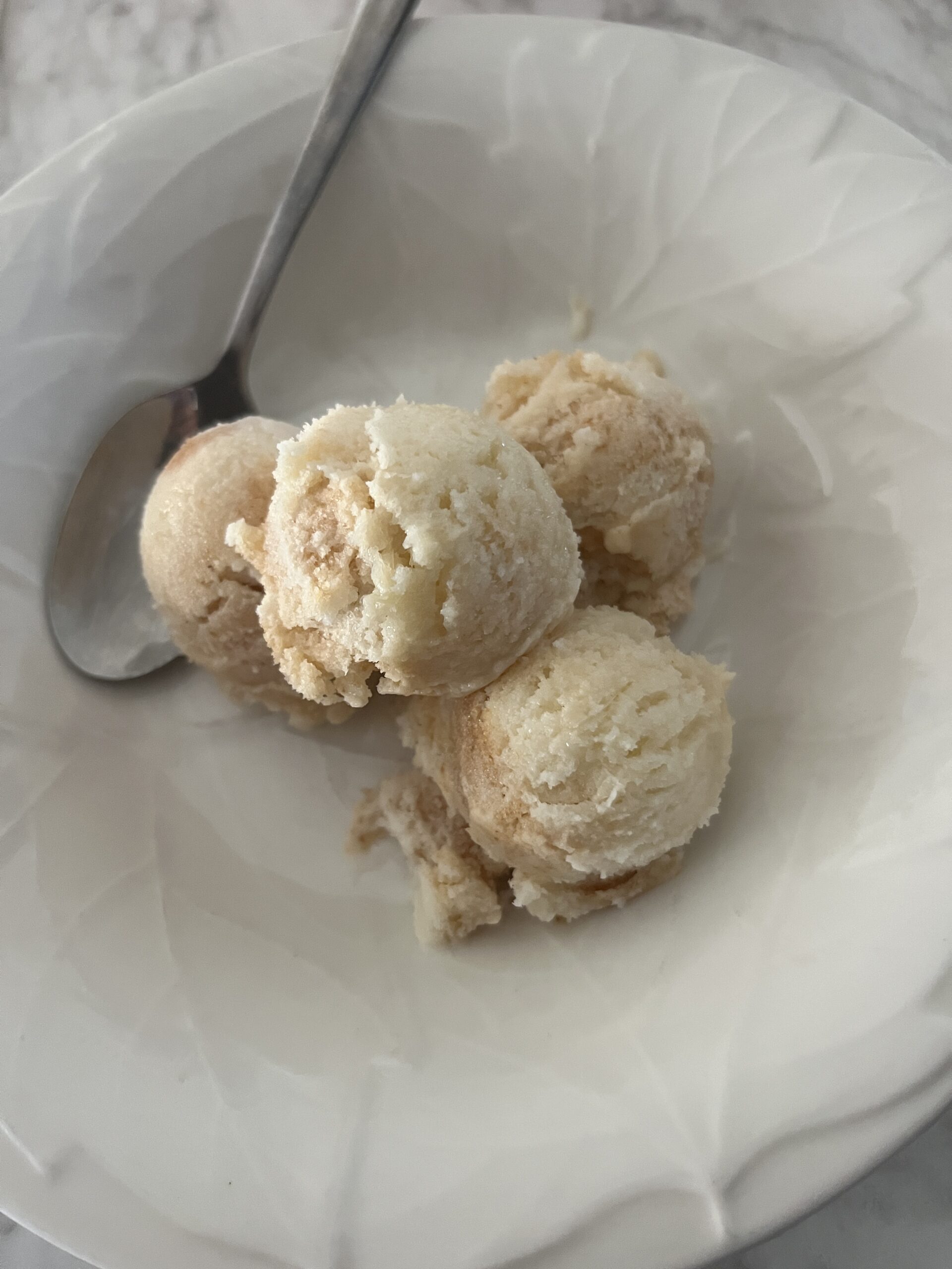 four scoops of ice cream inside of a white bowl with a silver spoon in the background just behind the ice cream
