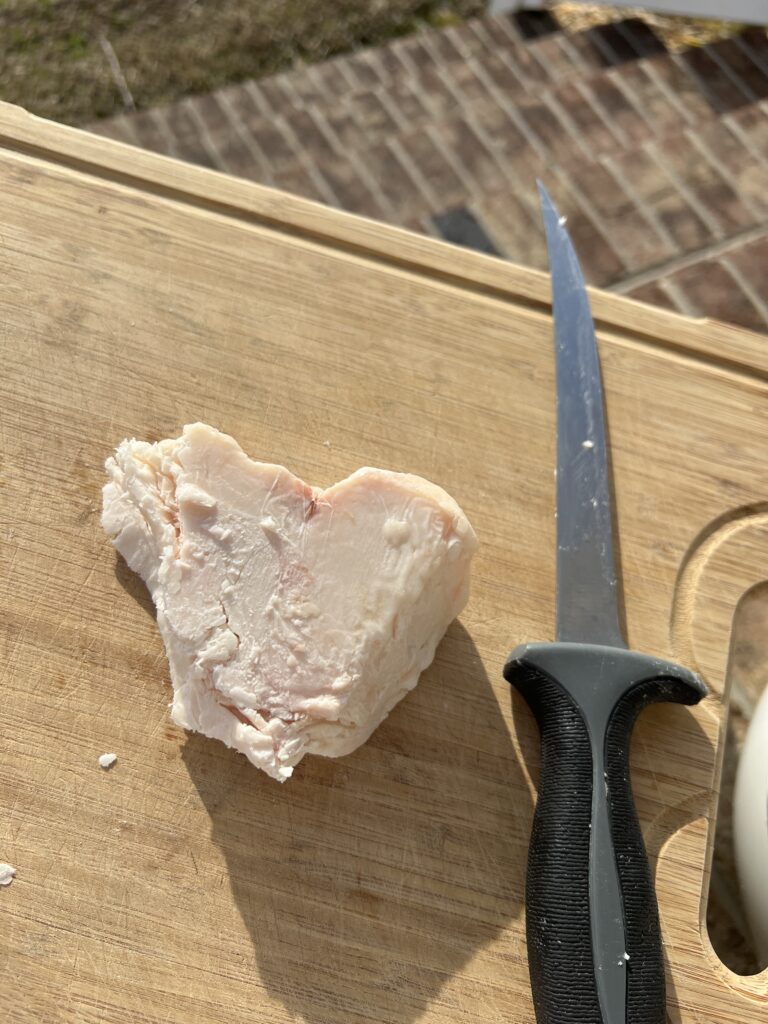 a heart shaped chunk of beef tallow on a bamboo cutting board with a filet knife beside it 