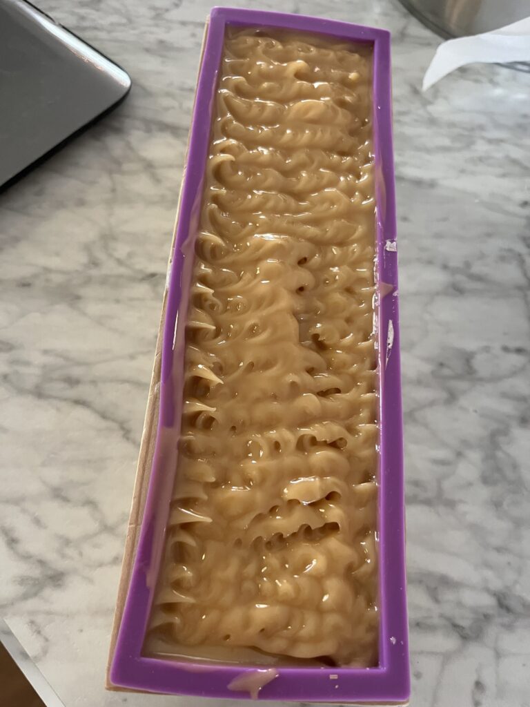 a loaf of wet tallow and goats milk soap in a purple soap mold with wavy designs in the soap