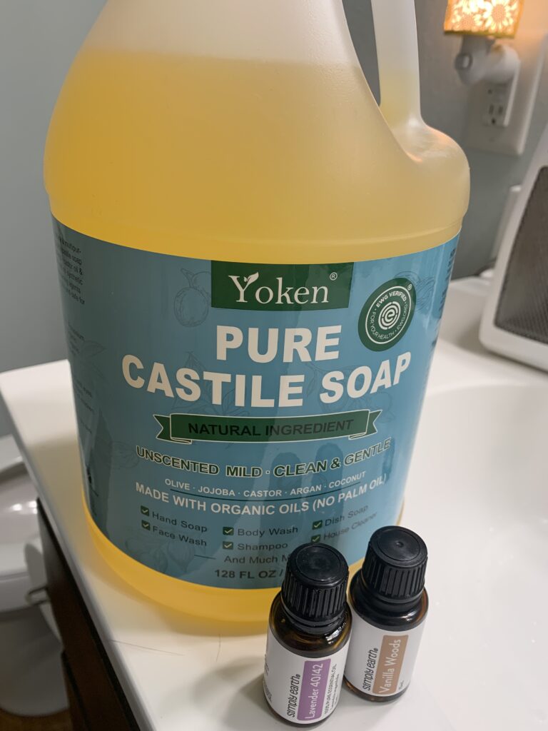 gallon bottle of liquid Castile soap sitting on a white counter with 2 amber bottles of essential oils standing in front