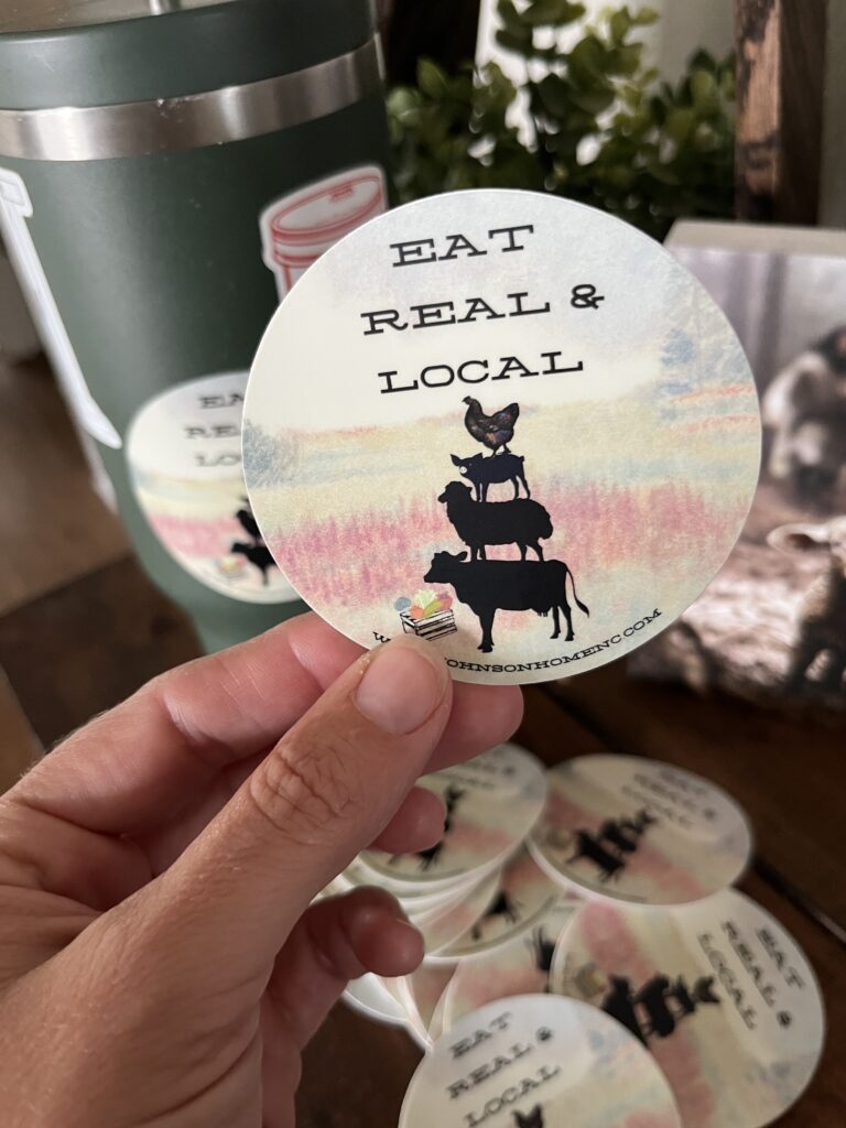 fingers holding an Eat Real & Local sticker designed by Johnson Home, LLC