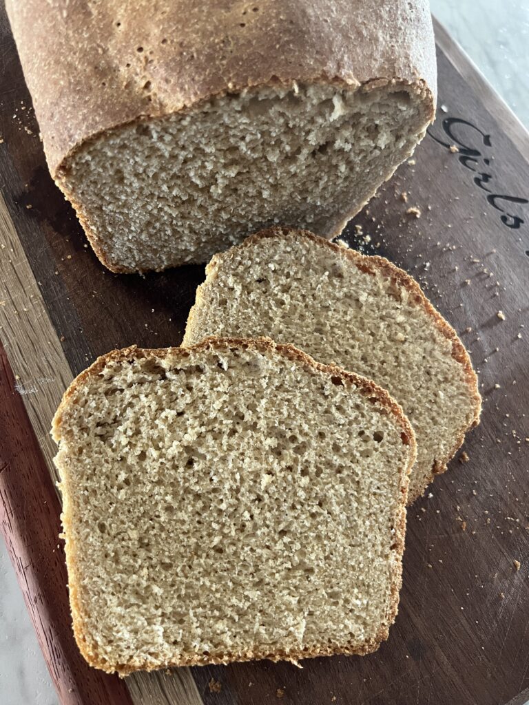 two slices of honey wheat bread on a wooden cutting board with the rest of the loaf in the background