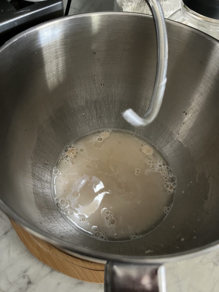 top view of yeast, water, and honey in a standing mixer with a dough hook lifted