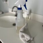 frosted plastic bottle with white and blue spray nozzle sitting on a white bathroom counter in front of a sink with a white rag on the counter in front of the all-purpose cleaner spray