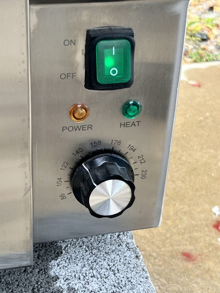 knobs and switches on a stainless steel machine indicating the temperature set and green light in the On position