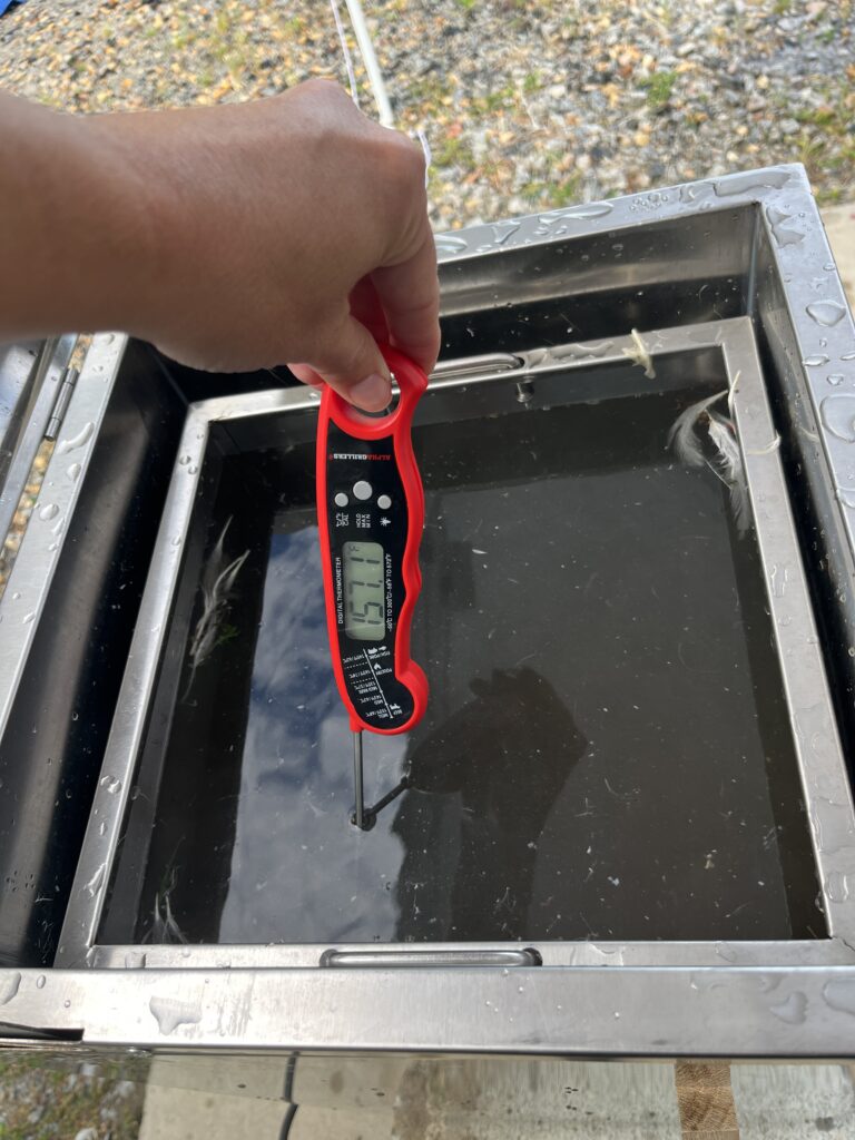 hand holding red stick thermometer in scalder of water