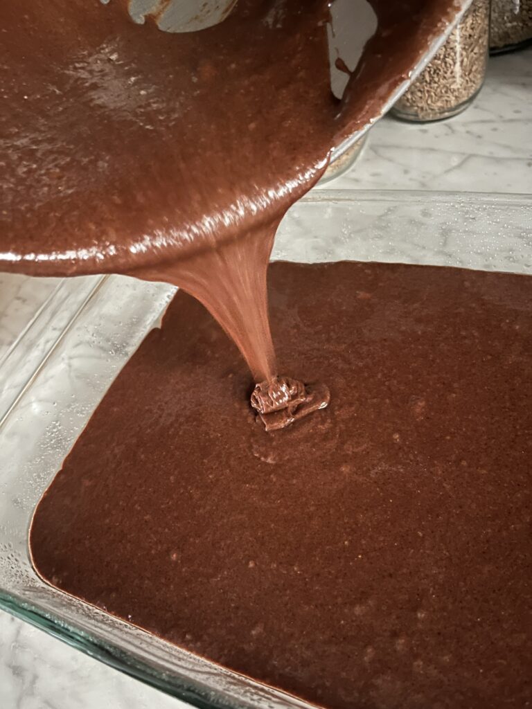 brownie batter being poured into a clear baking pan