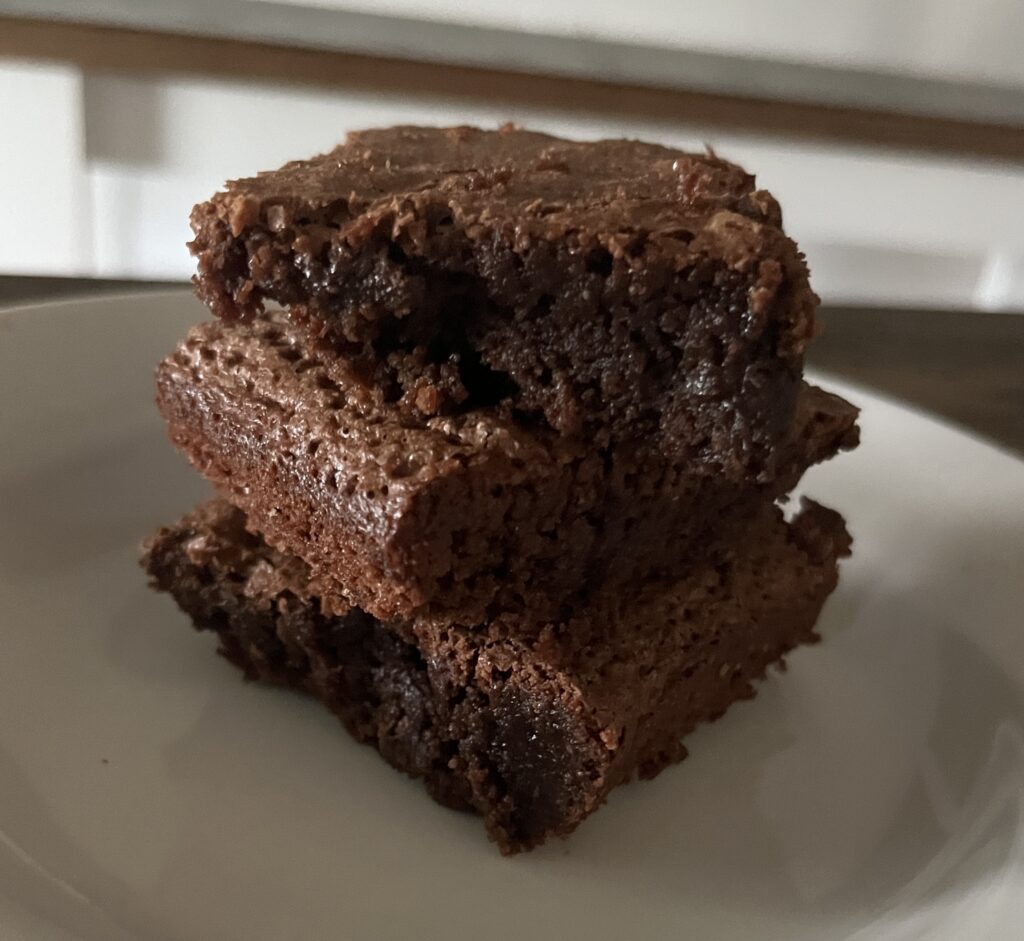 three freshly milled brownies piled up on a white plate