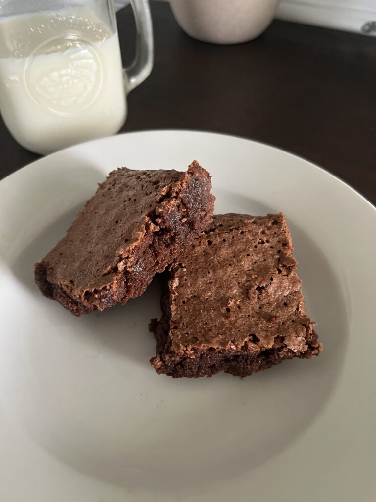 two freshly milled chocolate Brownies on a white plate with a mason jar of milk in the background