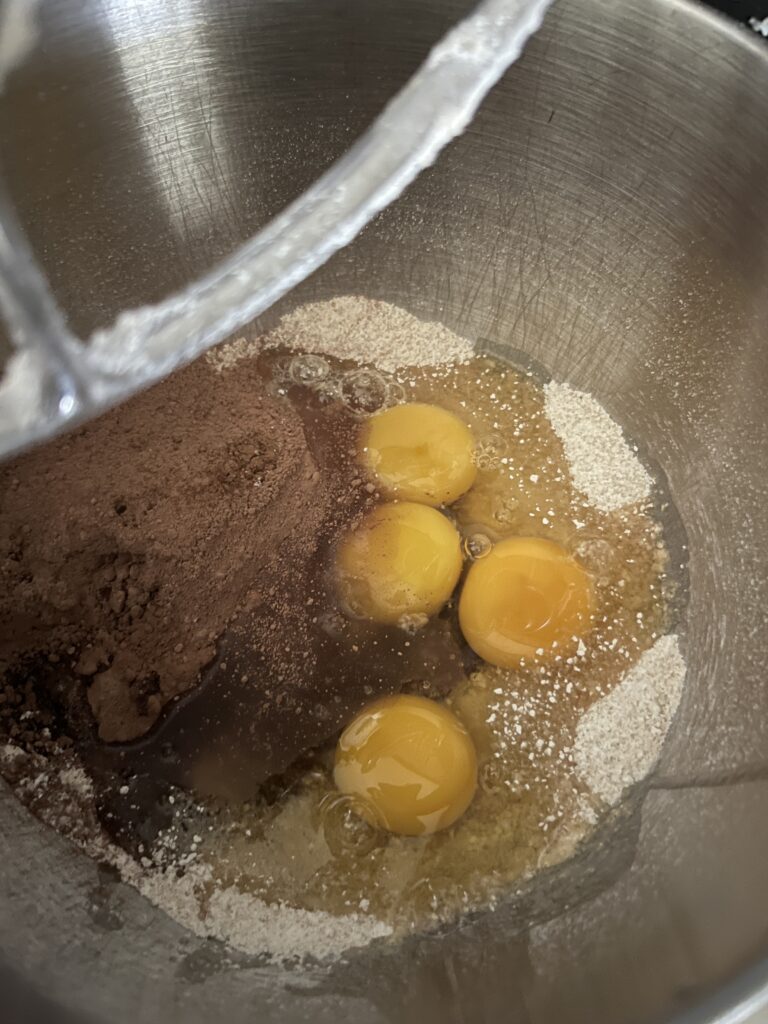 inside of a stainless steel bowl, 4 eggs, cacao powder, freshly milled flour, and other ingredients to make freshly milled brownies