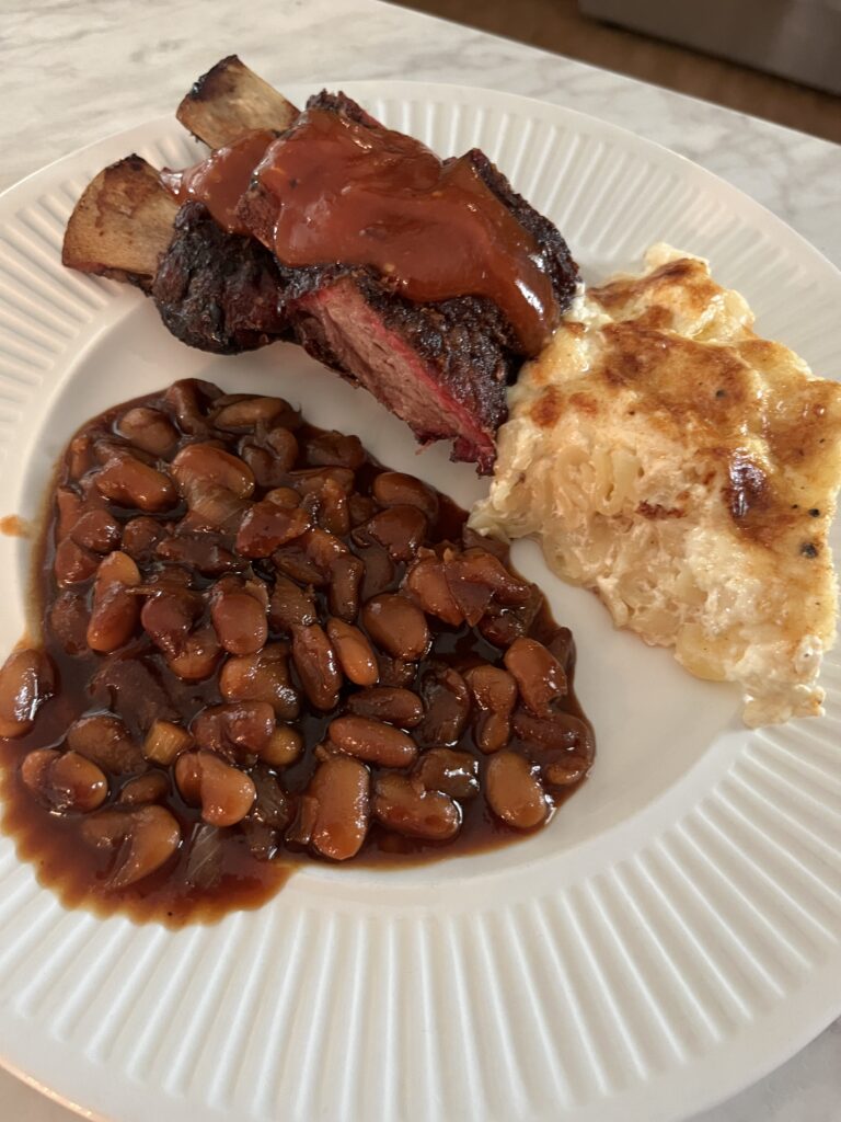 white plate of baked beans, short ribs, and macaroni and cheese