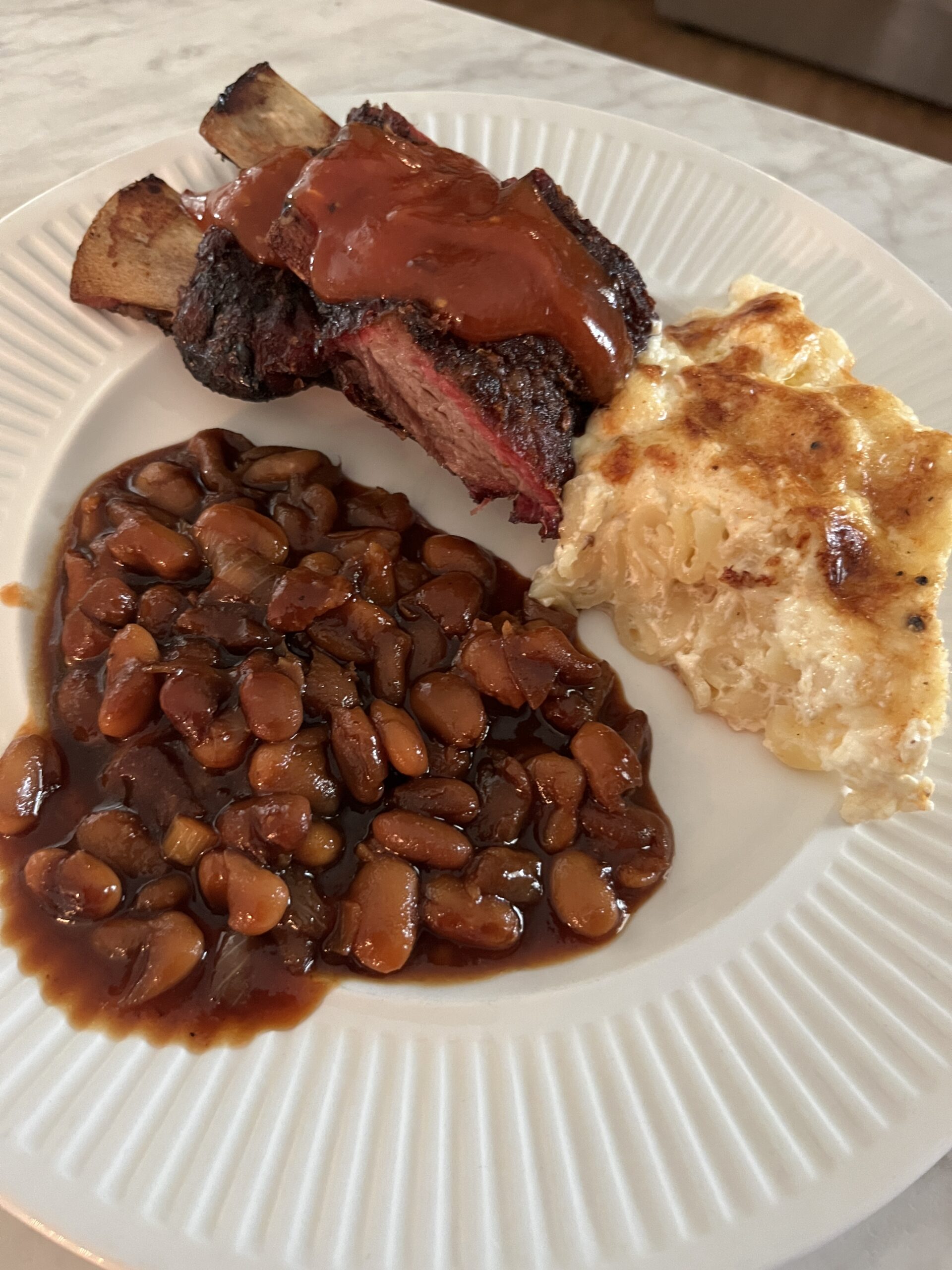 white plate of baked beans, short ribs, and macaroni and cheese