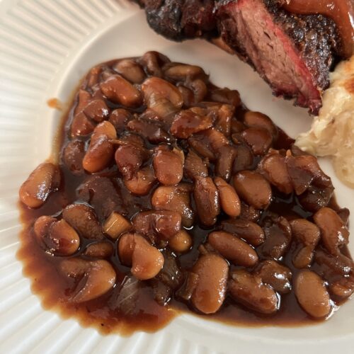 white plate holding homemade baked beans, short ribs, and macaroni and cheese