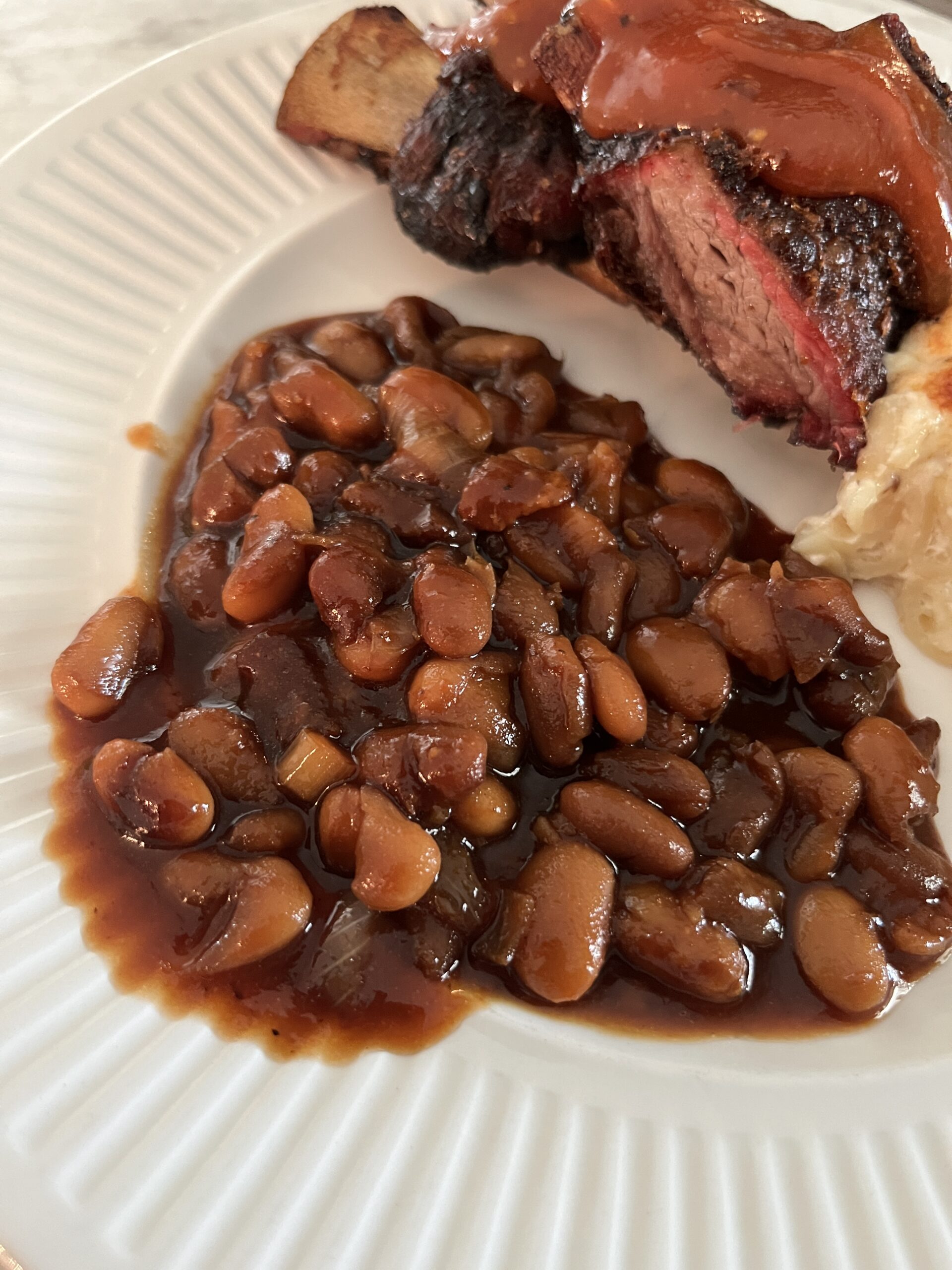 white plate holding homemade baked beans, short ribs, and macaroni and cheese