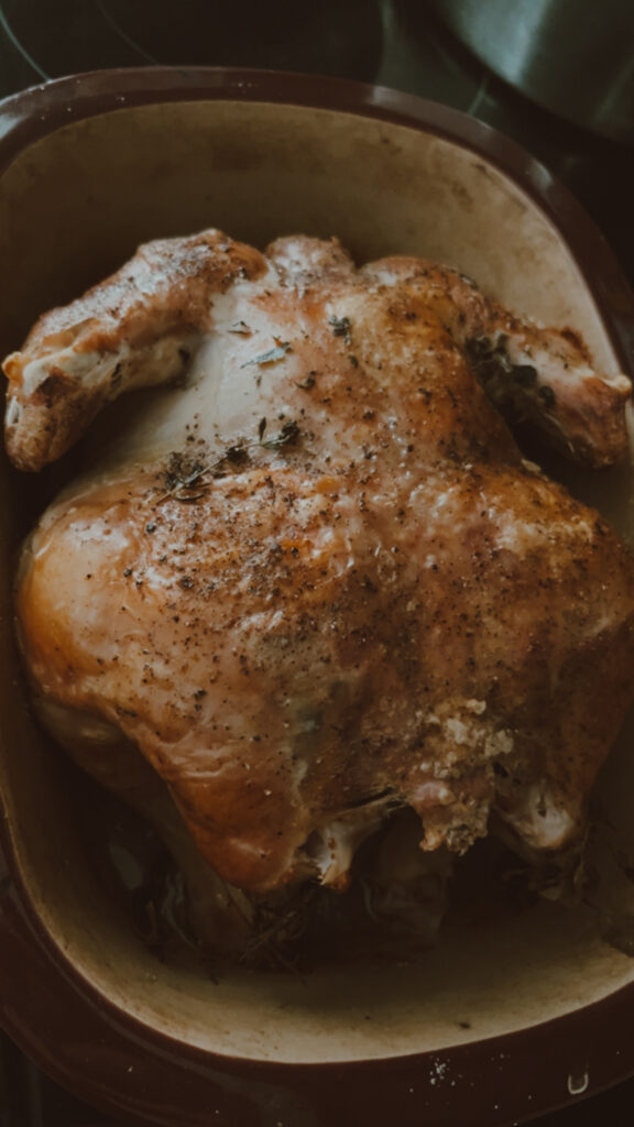 roasted whole chicken in a dark red roasting pan